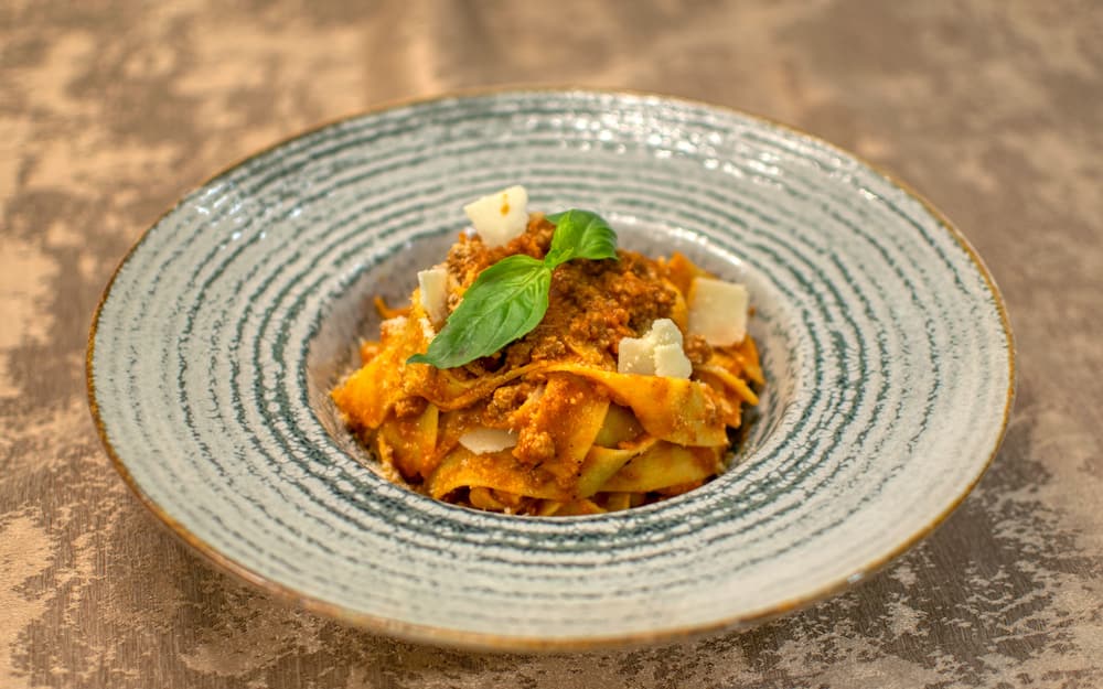 Pappardelle al ragù in un piatto bianco su tovaglia di lino